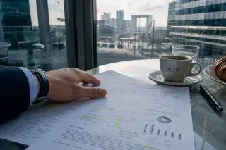 European investor's hand on an annotated financial report at a glass café table, Paris financial district visible through the window, cool late-afternoon light.